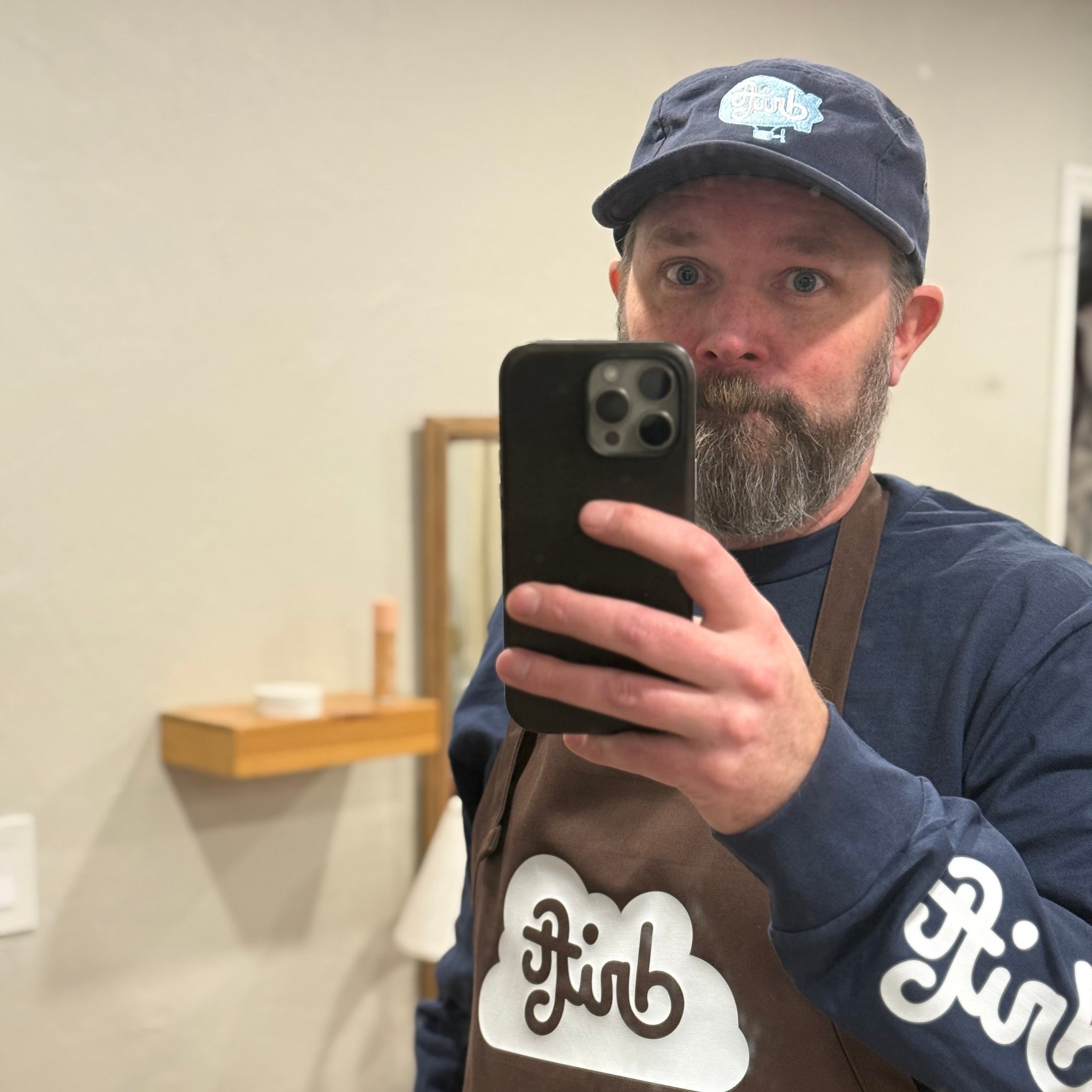 Brett Smith wearing a brown apron with 'drift' logo and a navy cap, taking a mirror selfie.